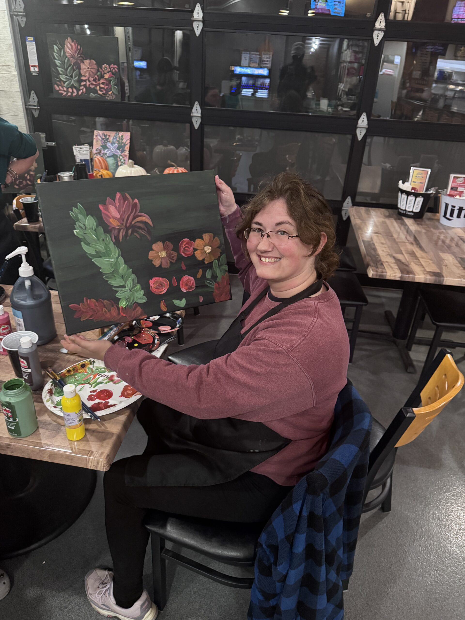 A guest holding her finished floral canvas at the Fall Boho Paint Series